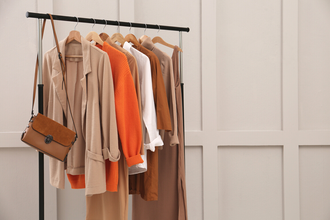 Rack with Stylish Women's Clothes and Bag near Light Wall. Space
